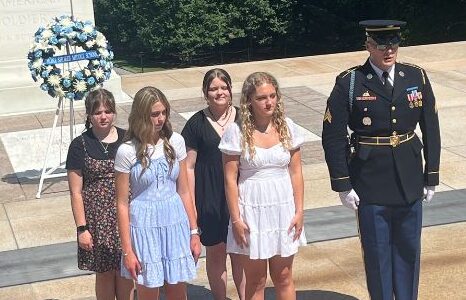 Four students stand with a Tomb Guard beside their wreath before a wreath-laying ceremony at the Tomb of the Unknown Soldier